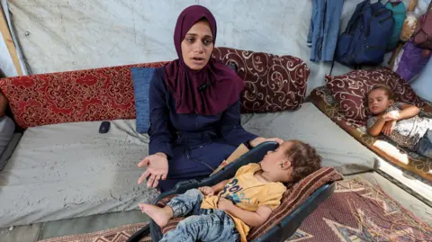 Reuters The mother of Palestinian boy Abdul Rahman Abu Al-Jidyan, who is the first person to contract polio in Gaza in 25 years, gestures as she looks after him in their tent, in Deir Al-Balah, in the central Gaza Strip August 28, 2024. 
