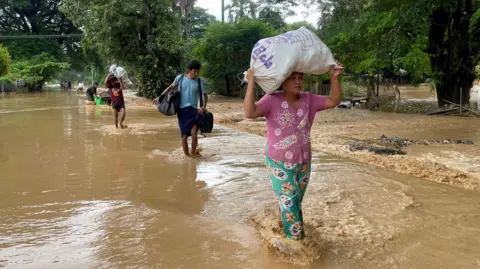 EPA People carry their belonging as they wade through flood waters in Pyinmana, Naypyidaw, Myanmar, on 13 September 2024.