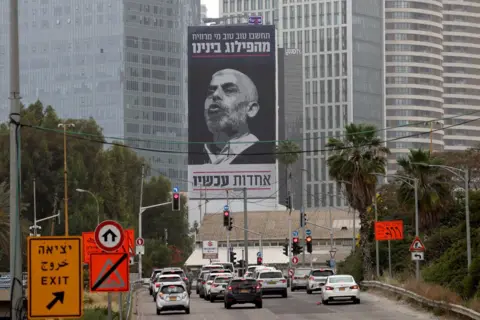 Getty Images Cars in Tel Aviv drive past a poster of Sinwar, with a message in Hebrew urging Israelis to unite against their most wanted enemy