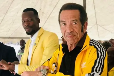 Innocent Selatlhwa Ian Khama in a yellow tracksuit points at his watch.