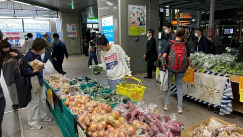 People are seen examining produce at a food stall in Urawa station, Japan