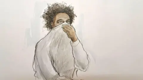 Helen Tipper A court drawing of Axel Rudakubana in the dock holding his sweatshirt up to cover his nose and mouth.