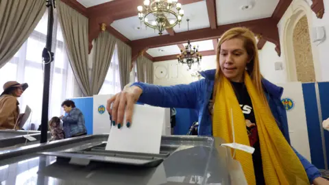 EPA A woman with blond hair, wearing a yellow scarf and a blue jacket, is seen casting her vote at a polling station