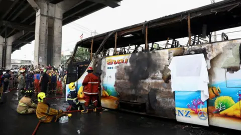 Reuters Firefighters work to extinguish a burned out school bus