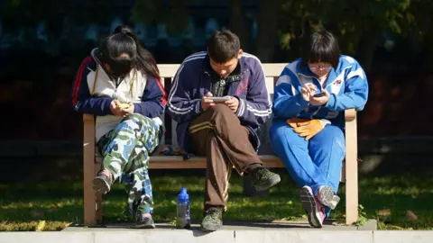 Getty Images A group of Chinese young people play on their mobile phone as they rest on a bench at a park in Beijing on November 7, 2013