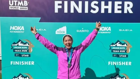 Fatima Painda Fatima Painda wearing a pink jacket and a medal around her neck, posing with her hands in the air