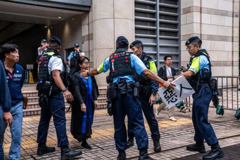 Getty Images Police officers remove a protest banner from Elsa Wu, the foster mother of one of the defendants Hendrick Lui, as she leaves the West Kowloon Court following a sentencing hearing for 45 pro-democracy activists in Hong Kong, China, on Tuesday, Nov. 19, 2024.