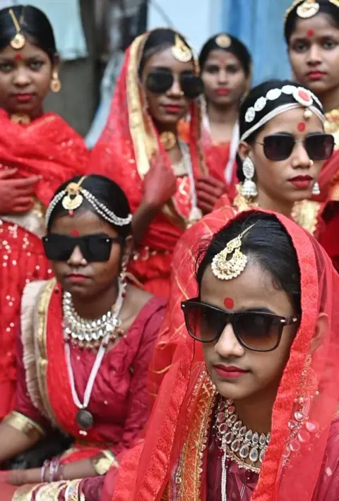 Innovation for Change Children model at a fashion show that has gone viral in India, close-up shot of seven girls in a group all wearing colourful red clothing, jewellery with Maang Tikka and sunglasses.