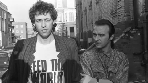 Getty Images An archive shot of Bob Geldof wearing a T-shirt that says 'feed the world' standing next to Midge Ure.