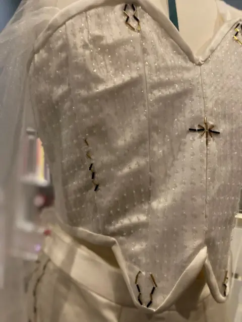 Jo White A beaded white corset with a cape in the background and trousers on a mannequin