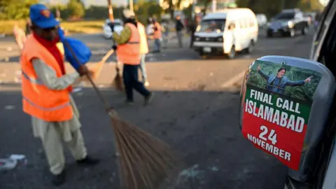 Getty Images Municipal workers clean the street leading to Red Zone area next to damaged vehicles after an overnight security forces operation against the supporters of jailed former prime minister Imran Khan's Pakistan Tehreek-e-Insaf (PTI) party in Islamabad on November 27, 2024. 