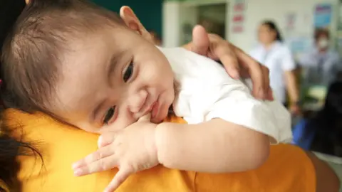 BBC/ Pritam Roy A baby lying on an adult's shoulder in a community centre in Valenzuela City, Manila