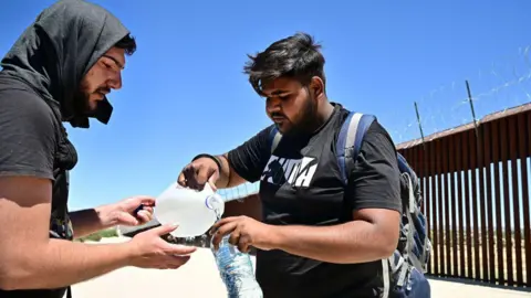 AFP Migrants from India share water in the intense heat after walking into the US from Mexico at Jacumba Hot Springs, California, on June 5, 2024. 