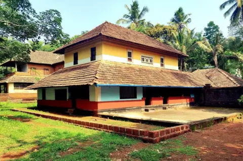 KK Gopalakrishnan A detached house surrounded by a low wall and some patchy grass