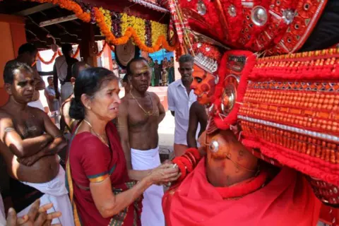 KK Gopalakrishnan A woman shakes the hand of a man wearing an elaborate red headdress