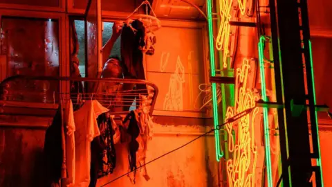 Getty Images A man hangs laundry next to a lit neon sign outside the window of his flat in Hong Kong on November 18, 2024.