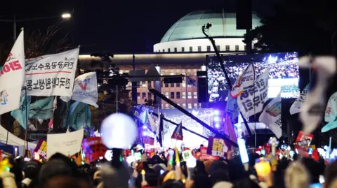 EPA Protesters hold candlelights and wave flags during a demonstration outside the South Korea national assembly. There is a festival atmosphere.