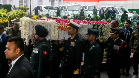 AFP via Getty Images Officers carrying a coffin draped in flowers and an Indian flag