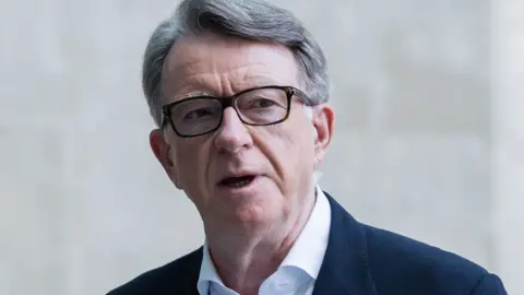 Getty Images A head shot portrait of Lord Mandelson taken against a neutral blurred background.  He is wearing glasses and a open collar white shirt with a dark jacket.