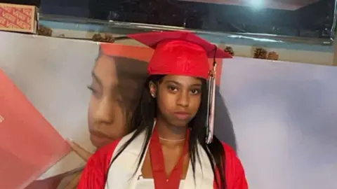 Melissa Dedeaux Nikyra Cheyenne Dedeaux wearing a red graduation cap and gown. Image is a close up, showing to just below shoulders.