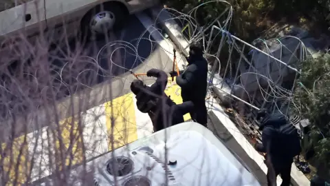 Reuters Police officers cut a wire fence set up at the entrance to the official residence of impeached South Korean President Yoon Suk Yeol, as authorities seek to execute an arrest warrant, in Seoul, South Korea, January 15, 2025.