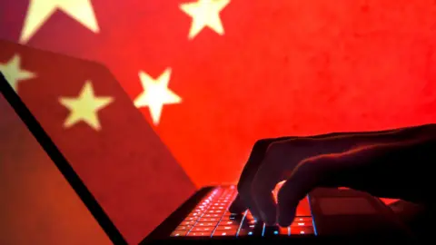 Getty Images hands in shadow typing on a computer in front of a Chinese flag