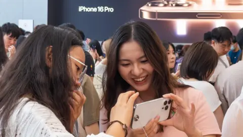 Getty Images Two young women look at an iPhone 16 Pro at an Apple Store in Chengdu, China.