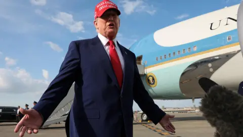 Reuters Trump in a suit and red MAGA cap talking to reporters on the tarmac at an airport on Florida on 16/2/2025