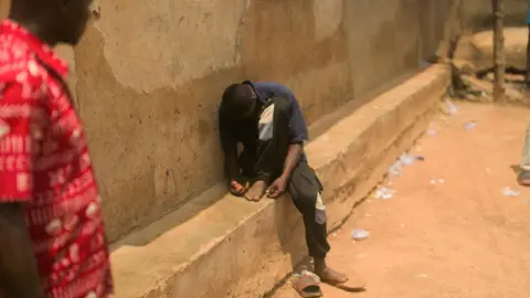 A young man sits on a ledge by a wall. He is slumped over so that his face cannot be seen. 