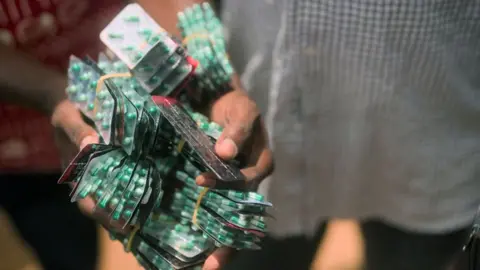 Hands holding more than 30 blister packs of green and white capsules.