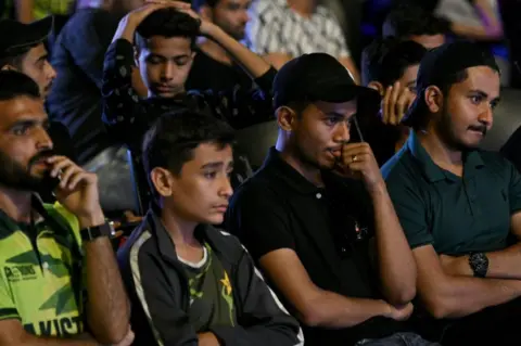 AFP Cricket fans react as they watch a live broadcast of the ICC Champions Trophy one-day international (ODI) cricket match between India and Pakistan in Dubai, on a big in Karachi on February 23, 2025