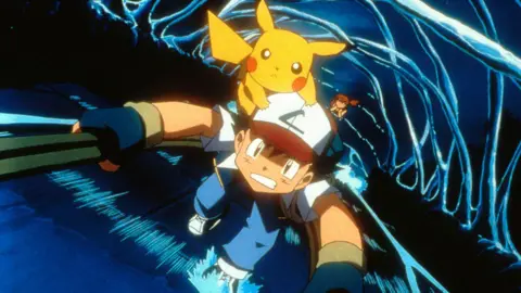 Getty Images Cartoon still shows Ash - a young boy in a white, red-peaked baseball cap, varsity jacket and wearing fingerless gloves - climbing a ladder as a swirling vortex of water rages below. Yellow, rodent-like Pikachu is clinging on to his cap, looking forward with determination.