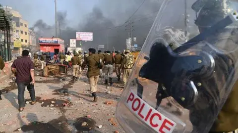 Getty Images Riot police walk along a road scattered with stones following clashes between supporters and opponents of a new citizenship law, at Bhajanpura area of New Delhi on February 24, 2020.