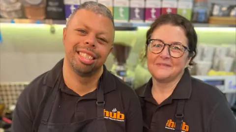 Ann-Marie Kinsman Reece and Penny standing next to each other, smiling. They are both wearing black uniforms saying The Hub in orange letters.