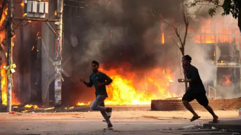 Getty Images Two men running on the road. Behind them is a store in flames.