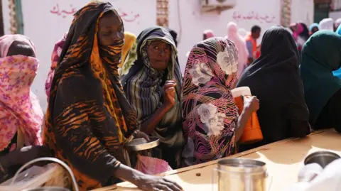 Getty Images Women in colourful headscarves wait in a queue for food to be distributed.