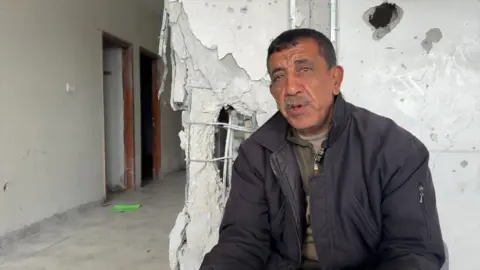 Marwan perches in front of a destroyed wall inside the corridor of a building