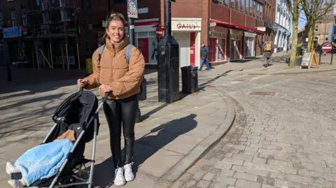 Stephanie Lamb with young child in a pushchair outside Gail's before it is open