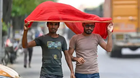 Getty Images The image shows two men using a red scarf to protect themselves from the heatwave during a hot summer afternoon in Delhi in 2024. 