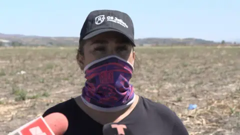 Luz Toscano speaks with her mouth covered and wearing a black baseball cap