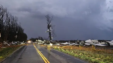 Missouri State Trooper Debris strewn across a road in Missouri, with storm clouds in the background.