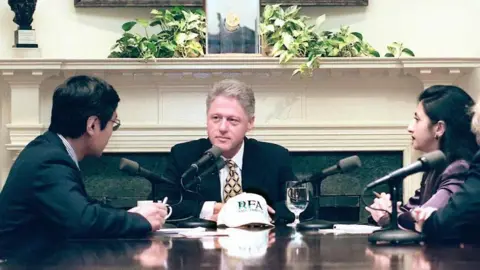 Getty Images US President Bill Clinton (centre) is interviewed by reporters L-R Feng Xiao Ming and Arin Basu from Radio Free Asia on 24 June at the White House in Washington DC. He is seated a table with the two reporters on his either side. 