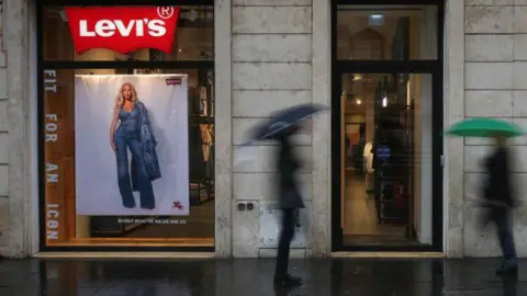 Getty Images Two men with umbrellas, blurred in the photo, walk past a shop selling Levi's jeans