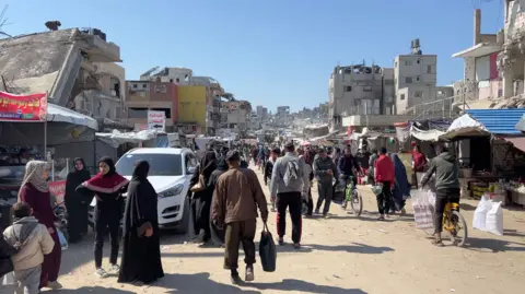 BBC Palestinians walk through a street market in Khan Younis, southern Gaza