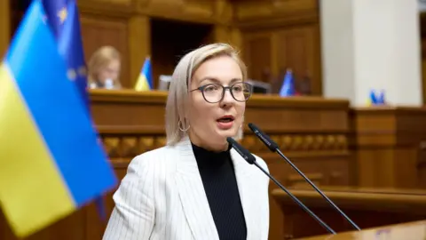 Inna Sovsun Inna Sovsun speaking in parliament in Kyiv with a Ukrainian flag behind her.